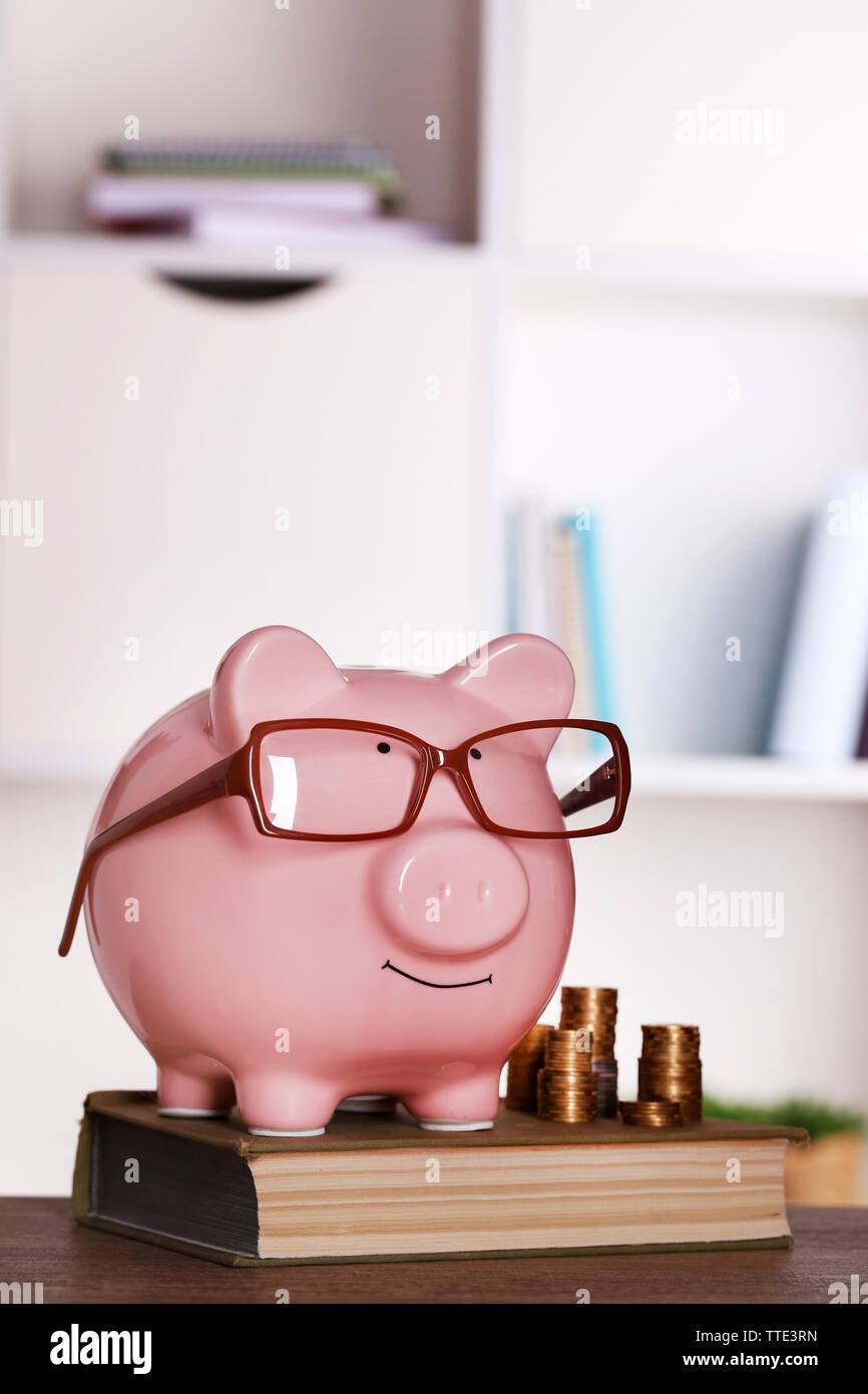 Piggy bank in glasses with book and coins on home or office background ...