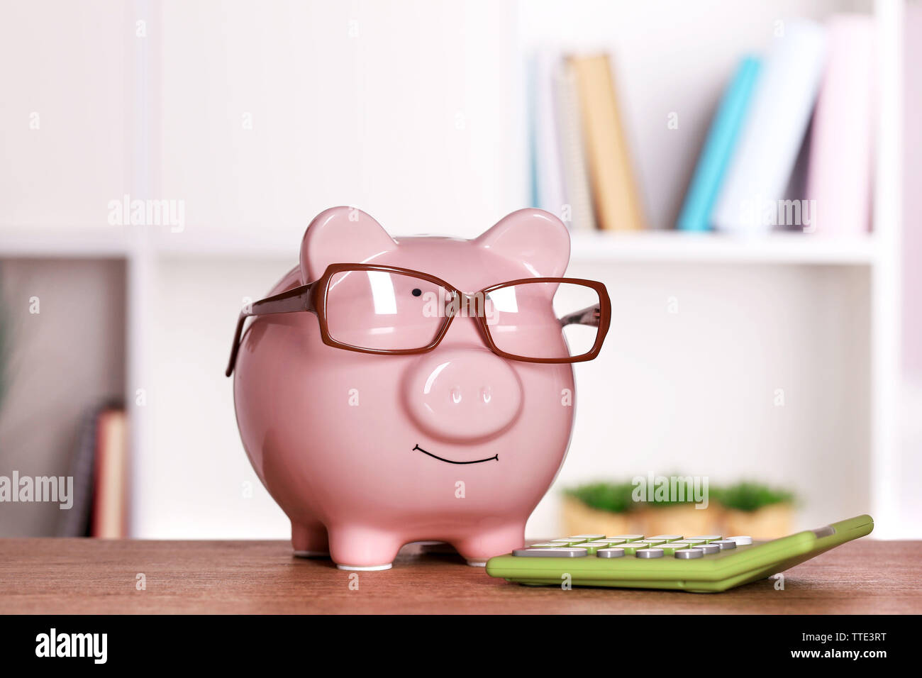 Piggy bank in glasses with calculator on home or office background ...
