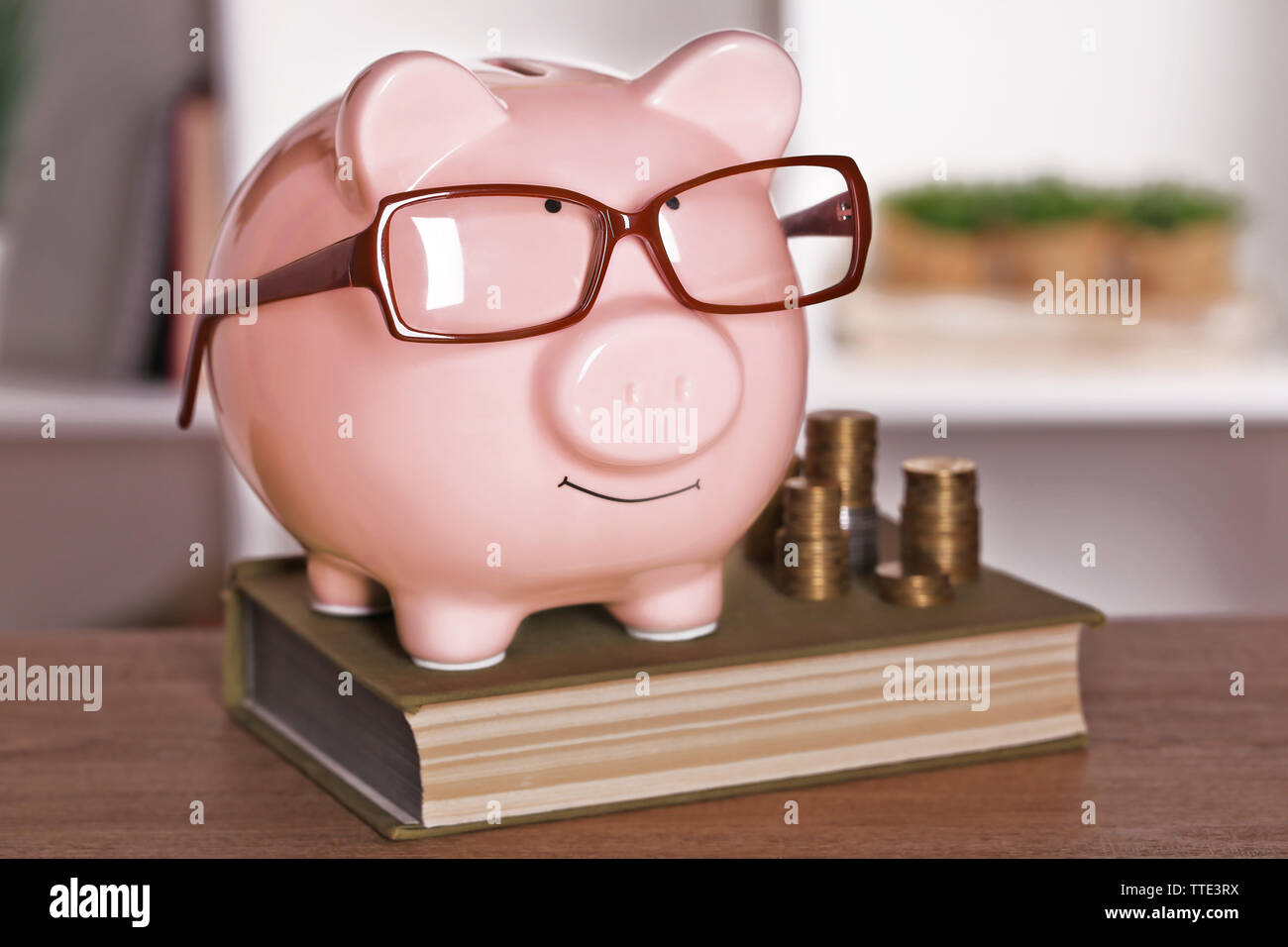 Piggy bank in glasses with book and coins on home or office background ...