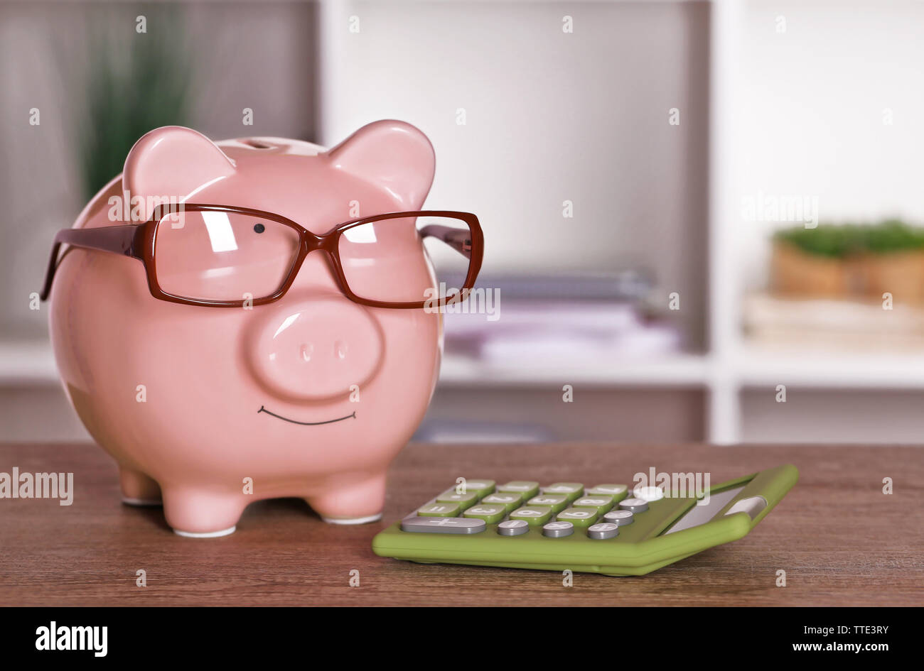 Piggy bank in glasses with calculator on home or office background ...