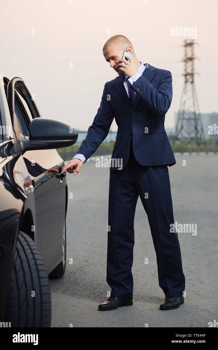 Young businessman in dark blue suit calling on cell phone next to his car Stock Photo