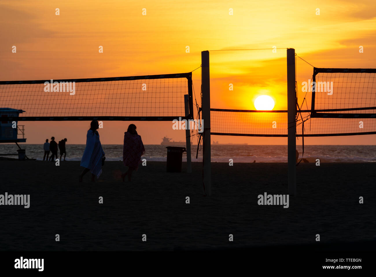Huntington Beach, CA / USA - March 25, 2019: Silhouettes of people enjoying the beach by the volleyball nets during a fiery and glowing sunset. Stock Photo