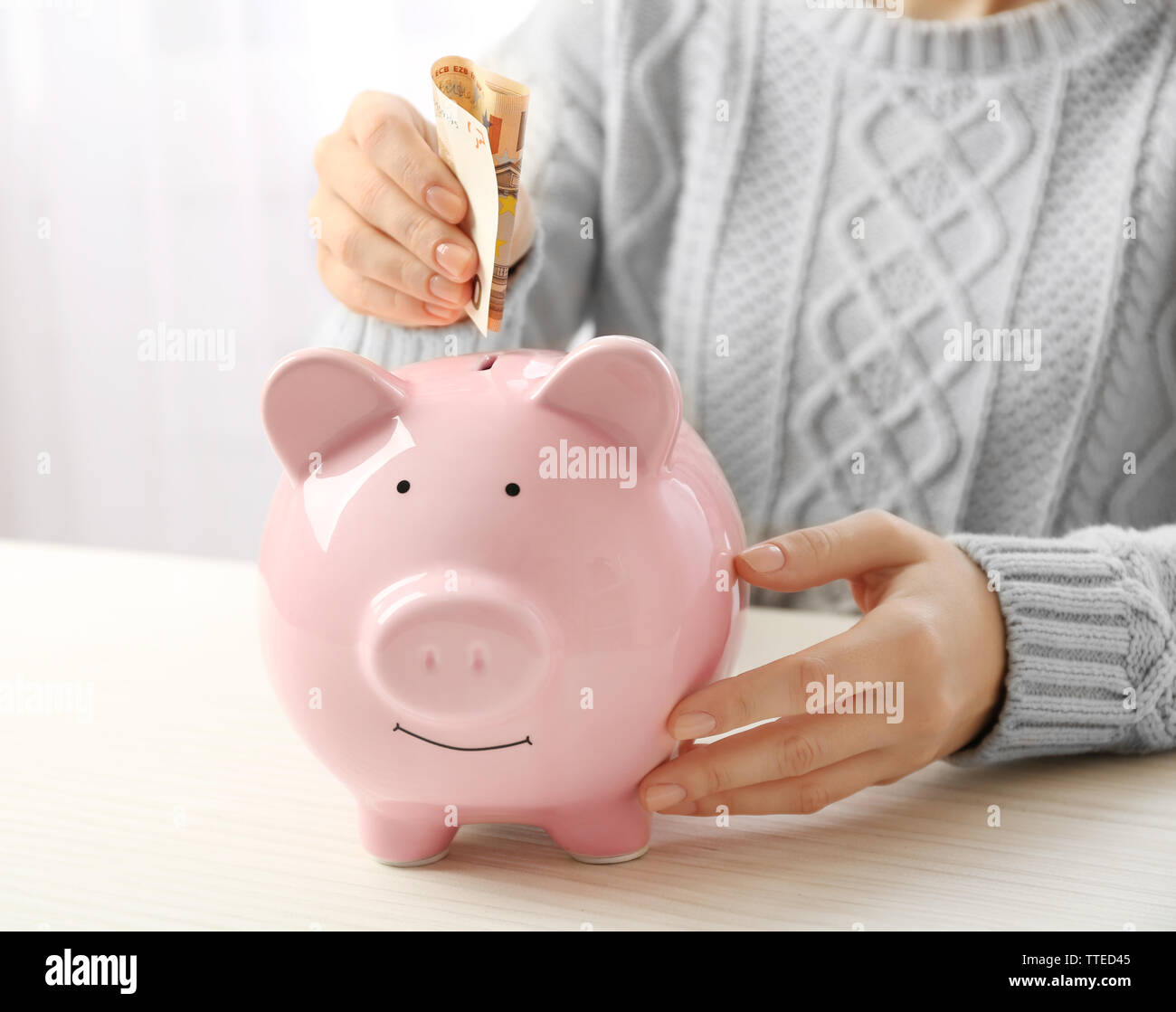 Woman putting euro banknote into a piggy bank on the table. Financial ...