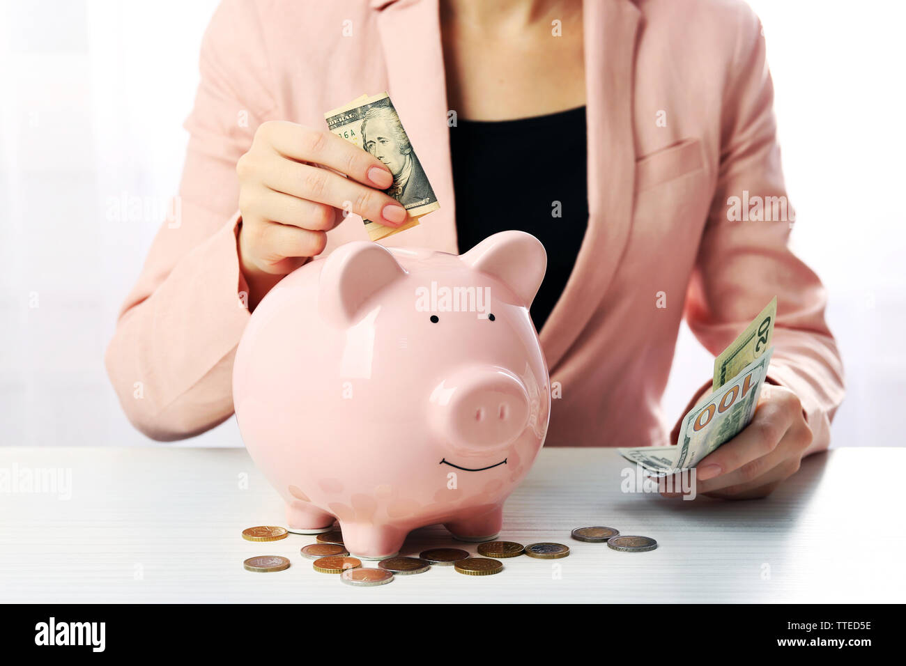 Woman putting dollar banknote into a piggy bank on the table. Financial ...