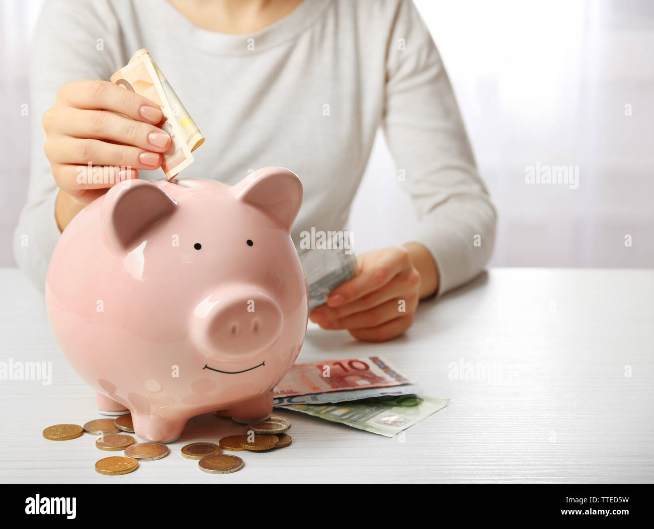Woman putting euro banknote into a piggy bank on the table. Financial ...