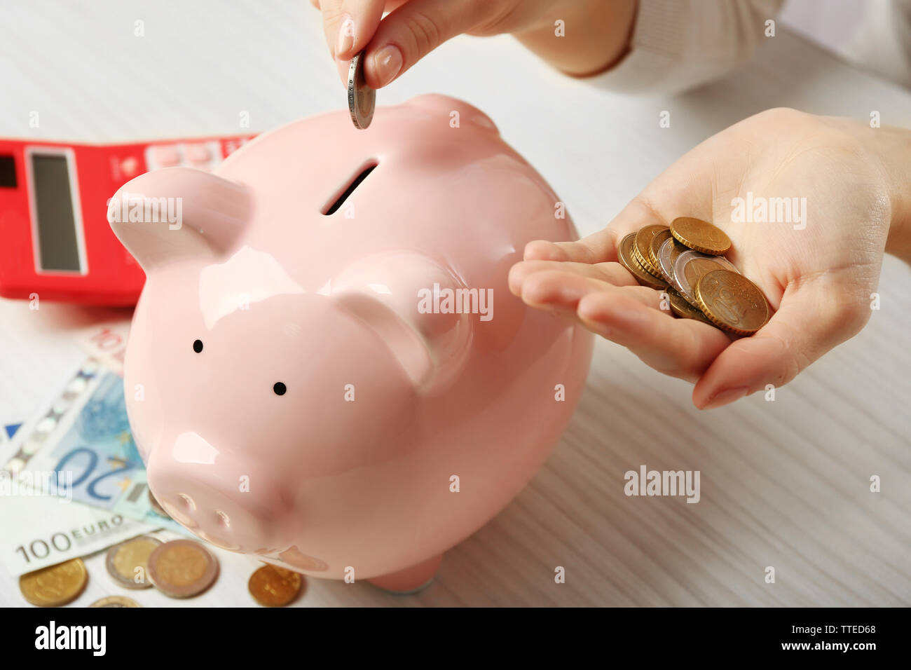 Woman's hands putting euro coin into a piggy bank on the table ...