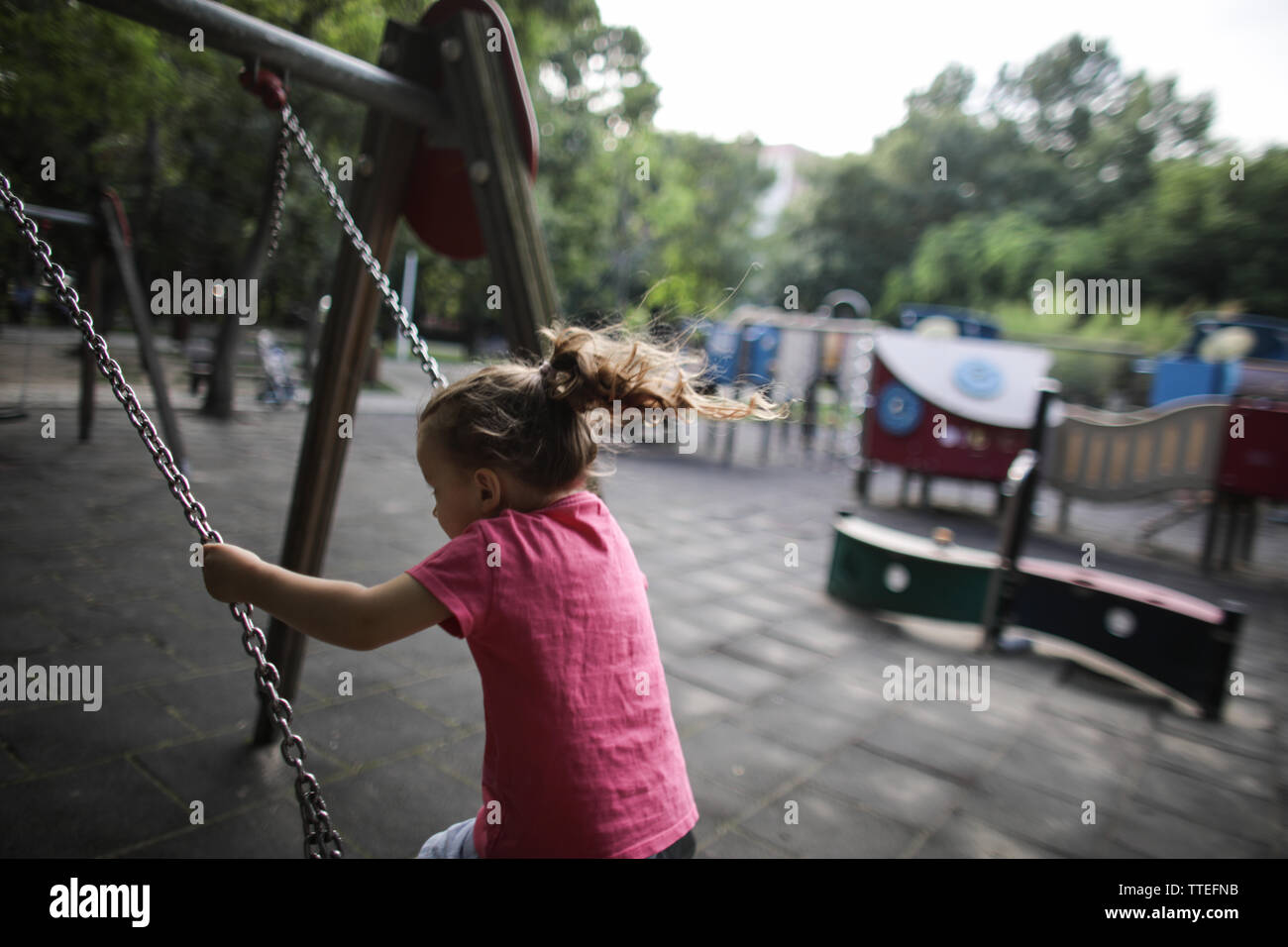 Young girl swinging in a kids playground without anyone around. Stock Photo