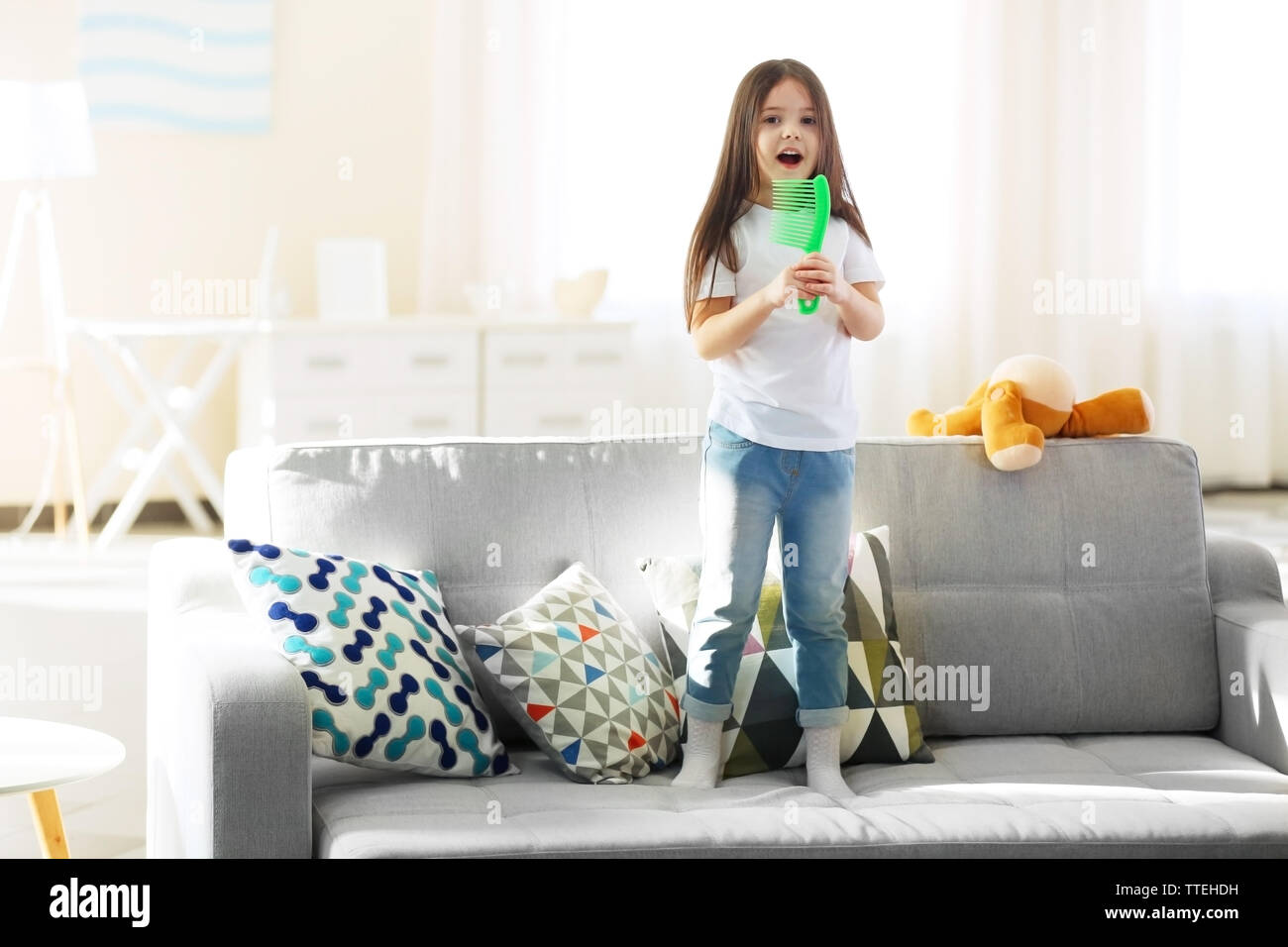 Beautiful Little Girl Singing In A Green Hairbrush On Sofa