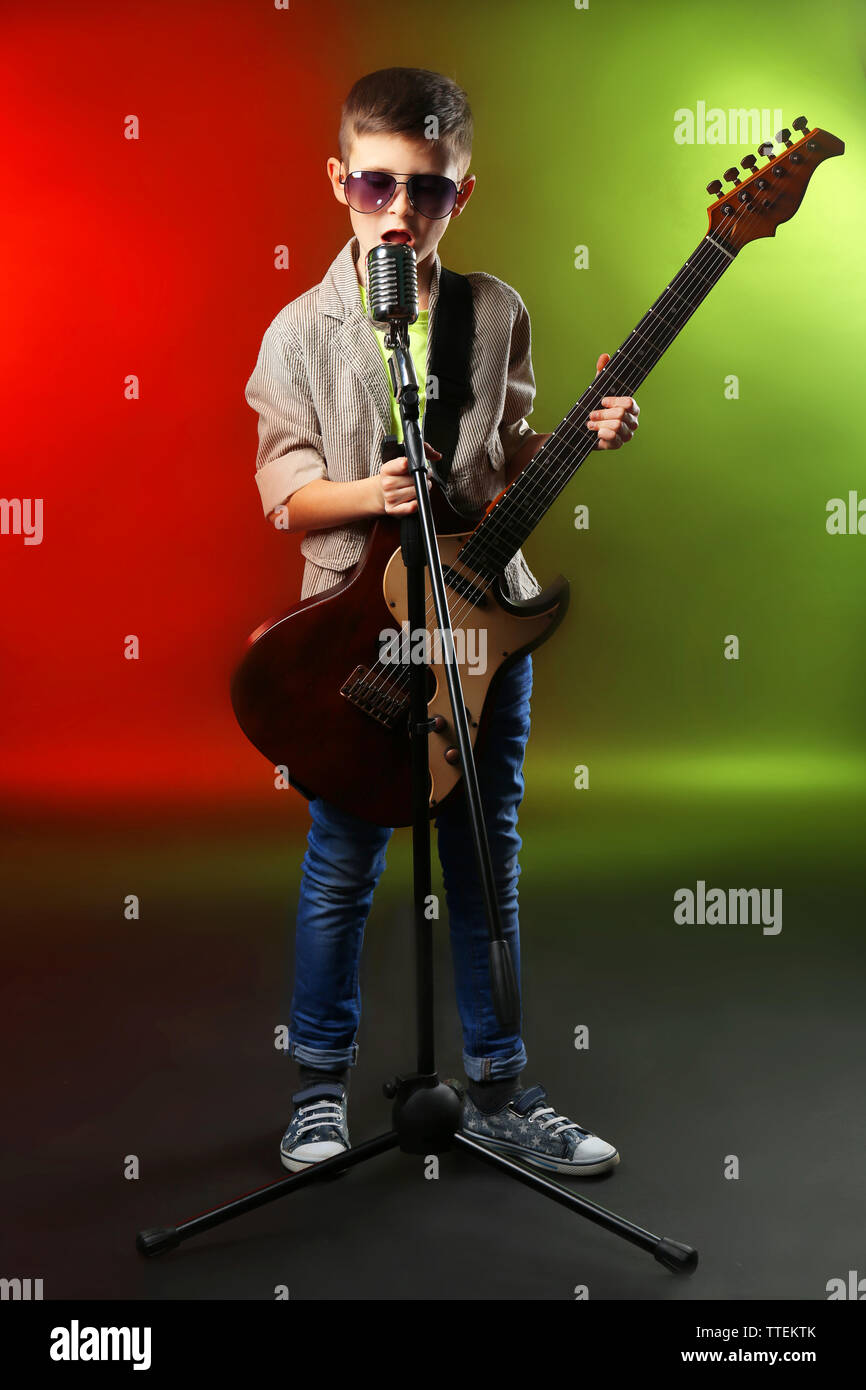 Little boy playing guitar and singing with microphone on a bright
