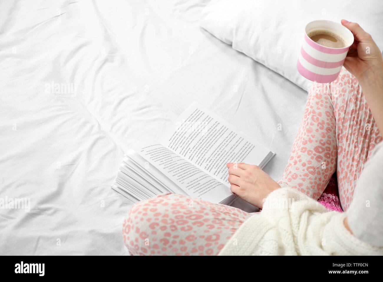 Woman in pajamas reading a book and drinking coffee on her bed Stock Photo  - Alamy