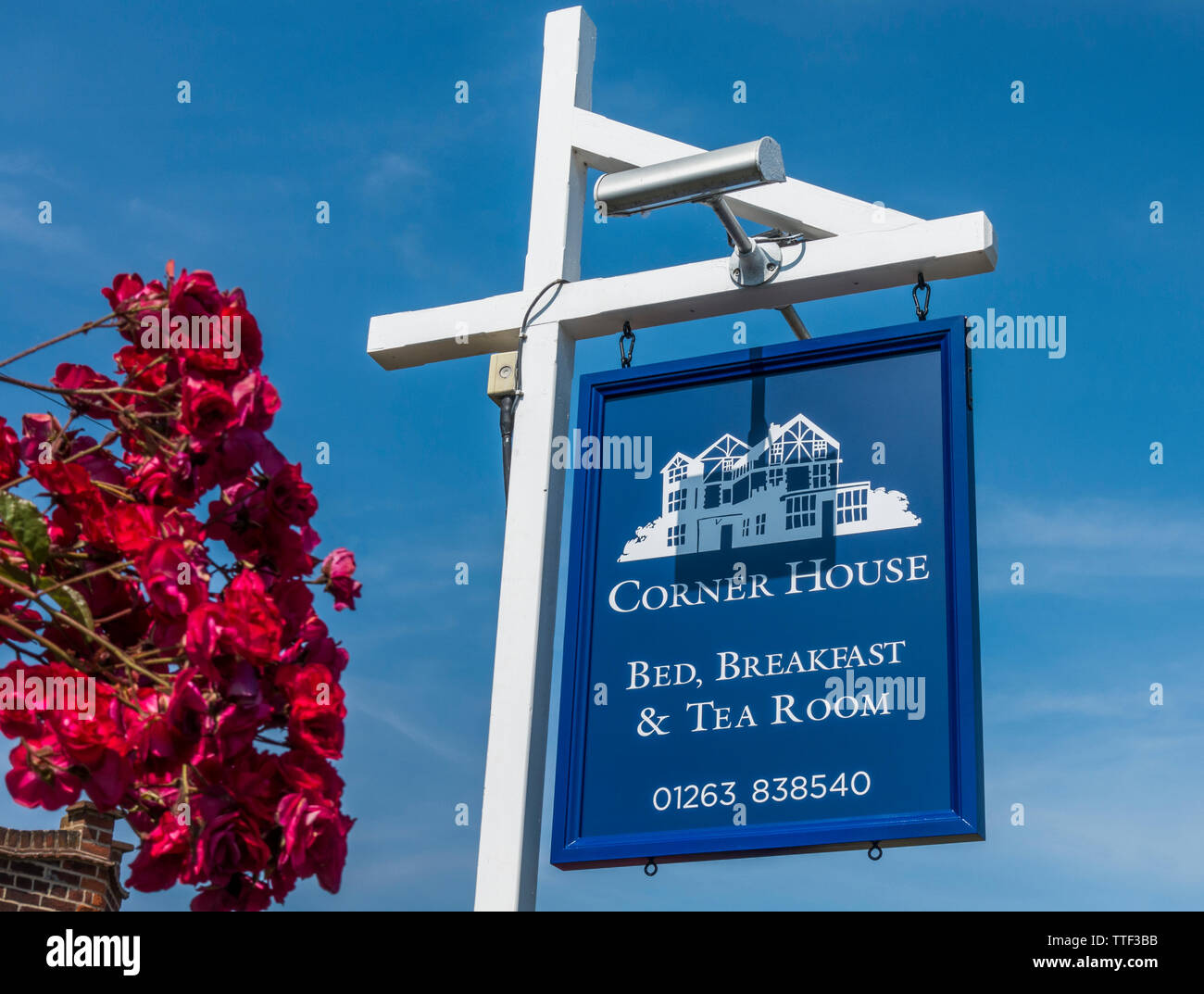 Blue sign with white woodwork, next to a pink rose bush, with blue sky