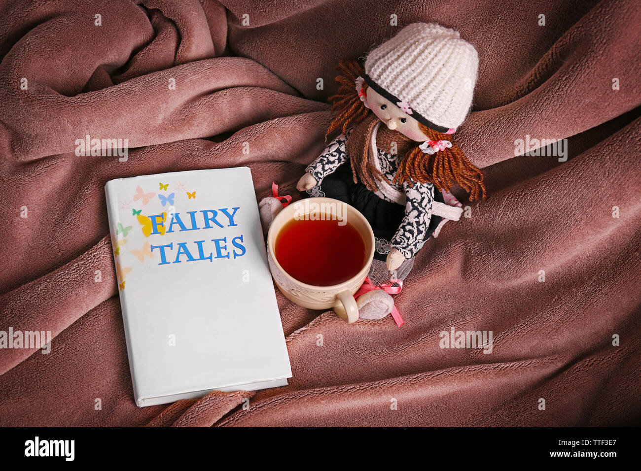 Rag doll with fairy tales book  and cup of tea on bedspread. Childhood concept Stock Photo