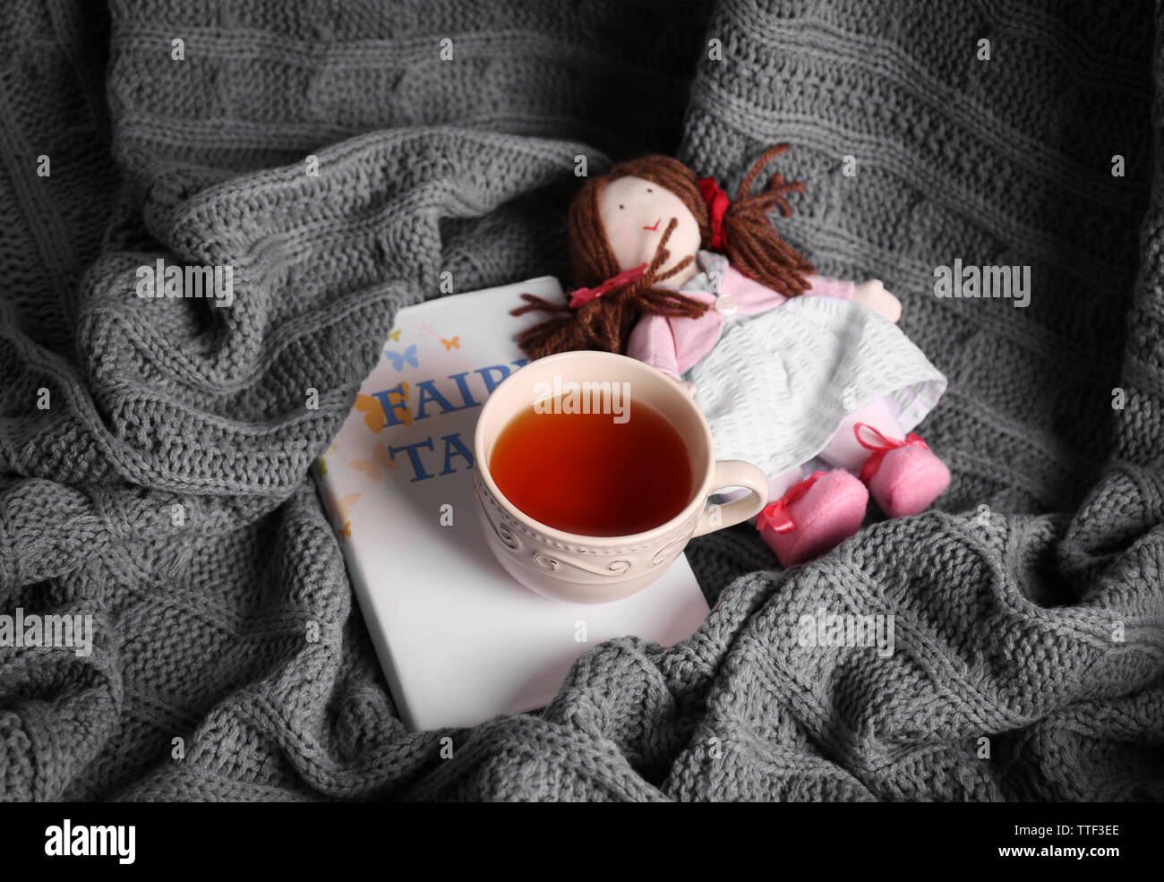 Rag doll with fairy tales book and cup of tea on bedspread. Childhood concept Stock Photo