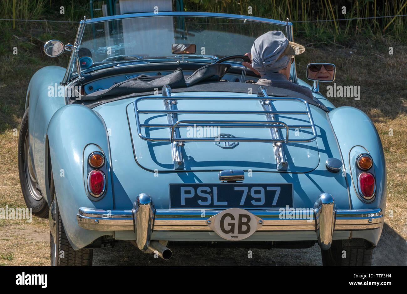 An elderly lady driver of a classic MGA, open top, British sports car, fully restored in pale blue paint, just about to drive off on a hot summer day. Stock Photo