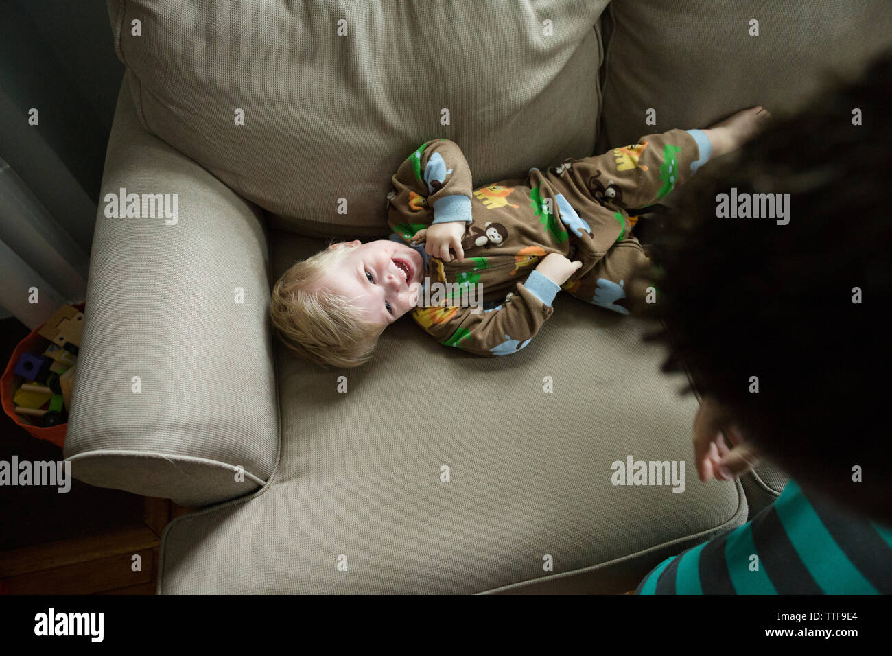 Laughing blonde toddler boy lays on couch at home smiling in pajamas Stock Photo