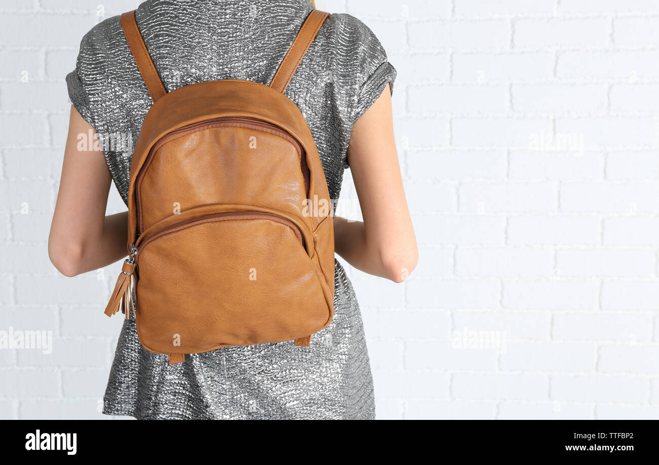 Back of woman with brown leather backpack against white brick wall background Stock Photo