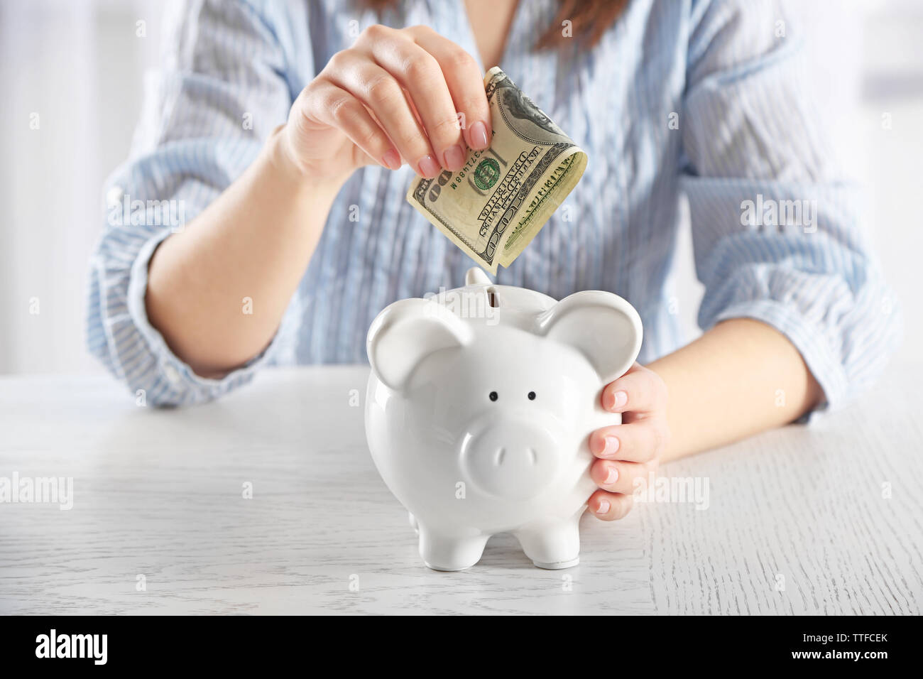 Woman sitting at table and putting money into piggy bank closeup Stock ...