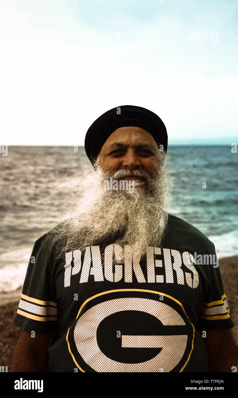 An old man with a long gray beard is standing by the sea. Stock Photo
