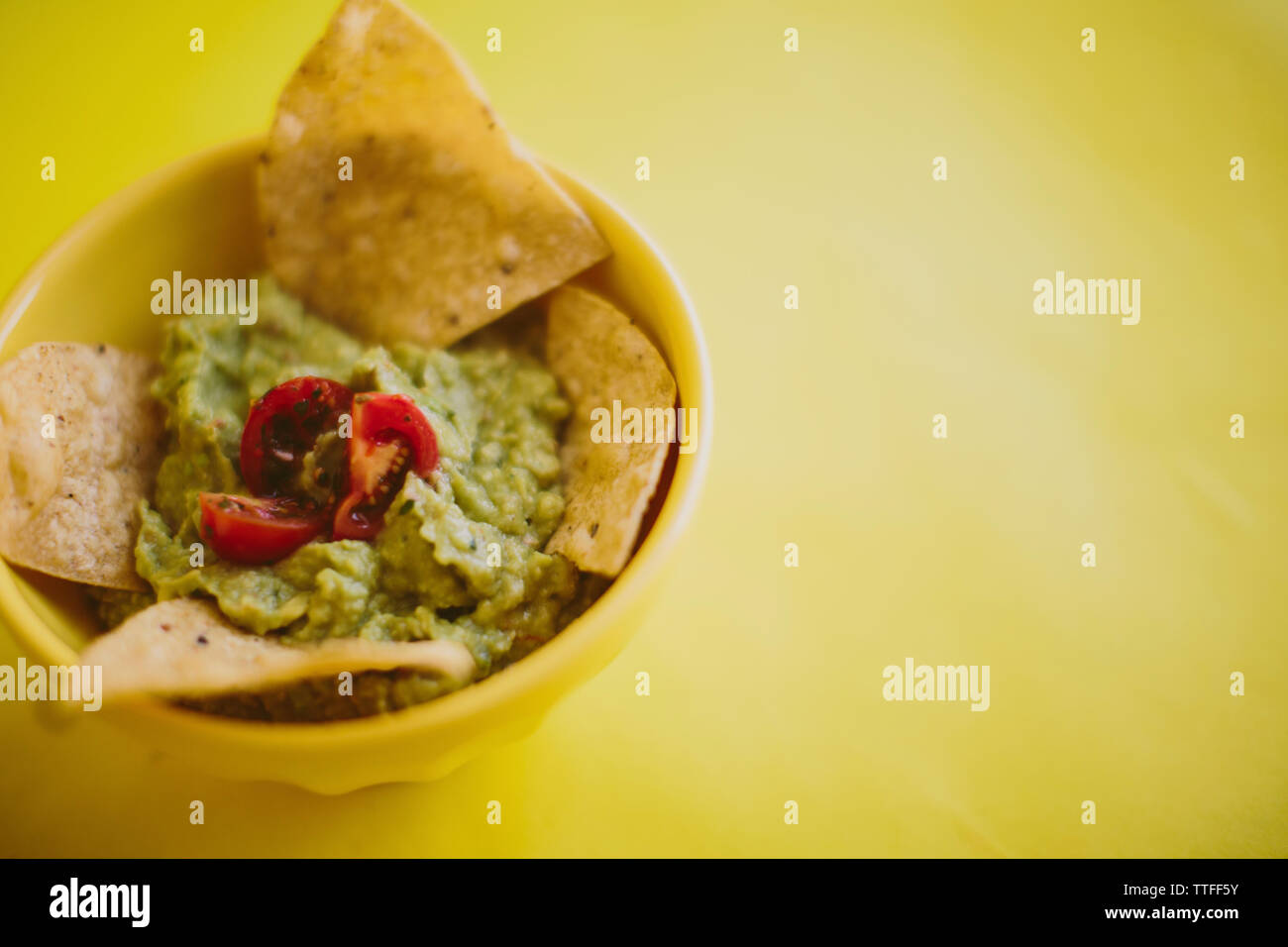 Close-up of guacamole with tortilla chips served in bowl over yellow background Stock Photo
