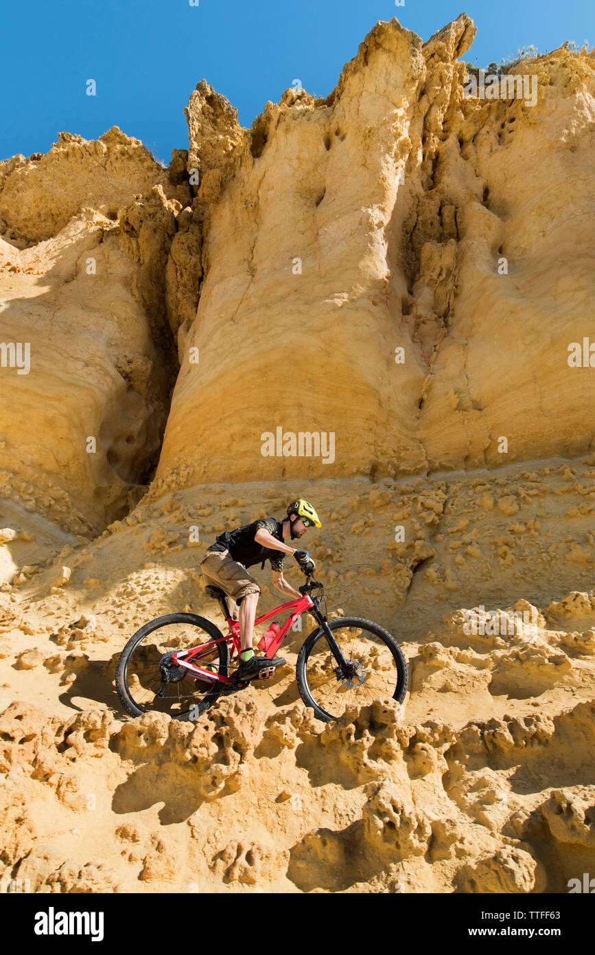 Low angle view of man cycling across vertical wall of sandstone Stock Photo
