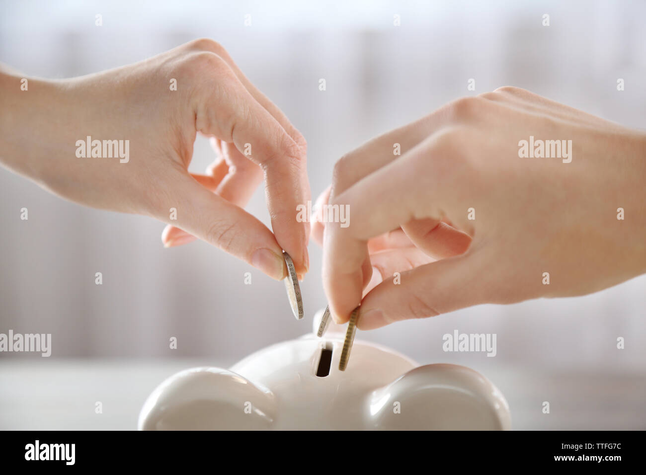 Hands putting coin into piggy bank at the table Stock Photo - Alamy