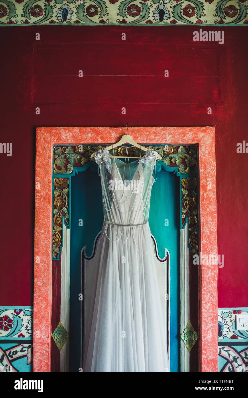 Beautiful white dress on hanger on traditional balinese textured red wooden door. Wedding concept. Stock Photo