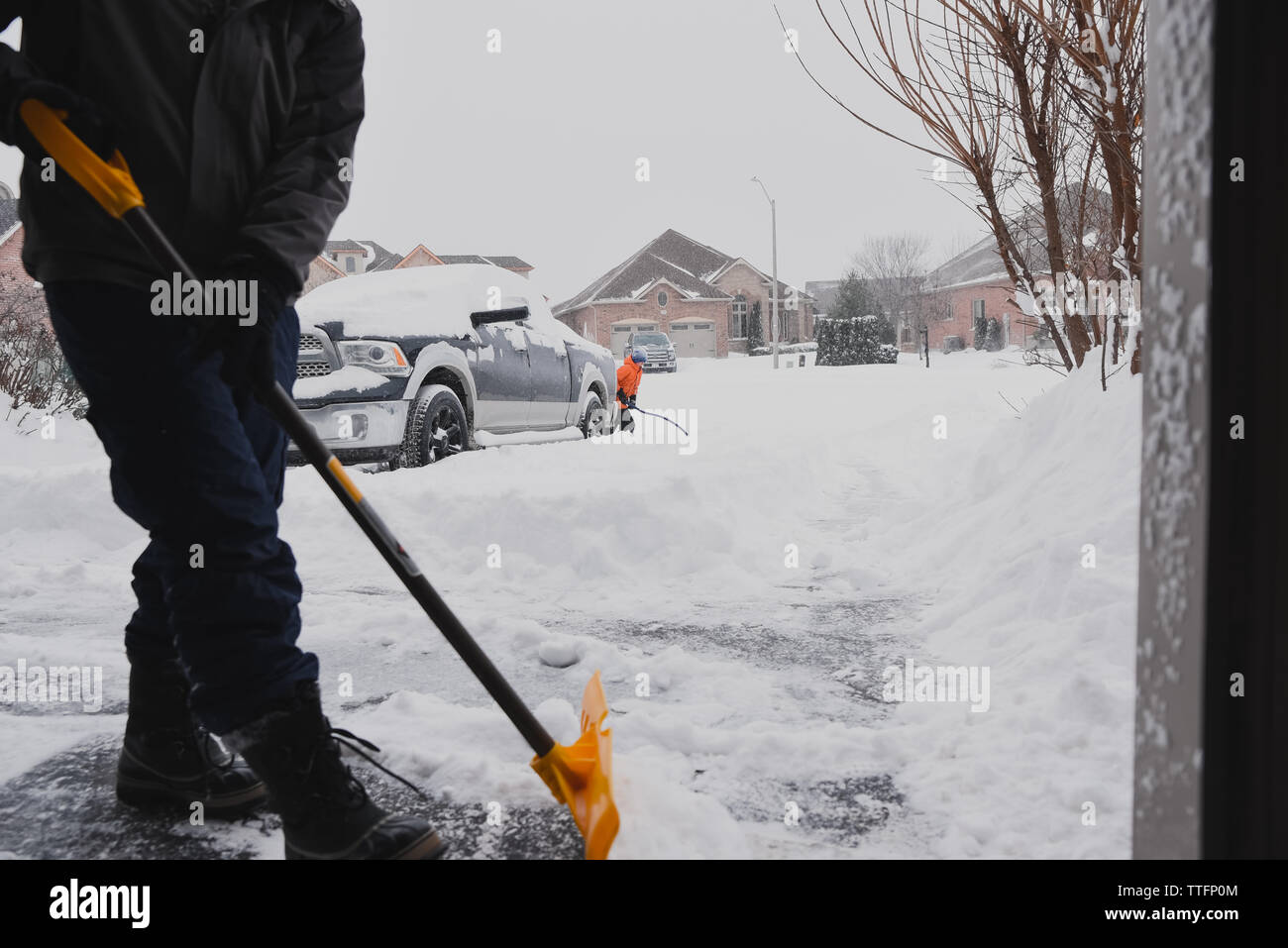 Man and child shovelling snow off of a driveway on a snowy day Stock