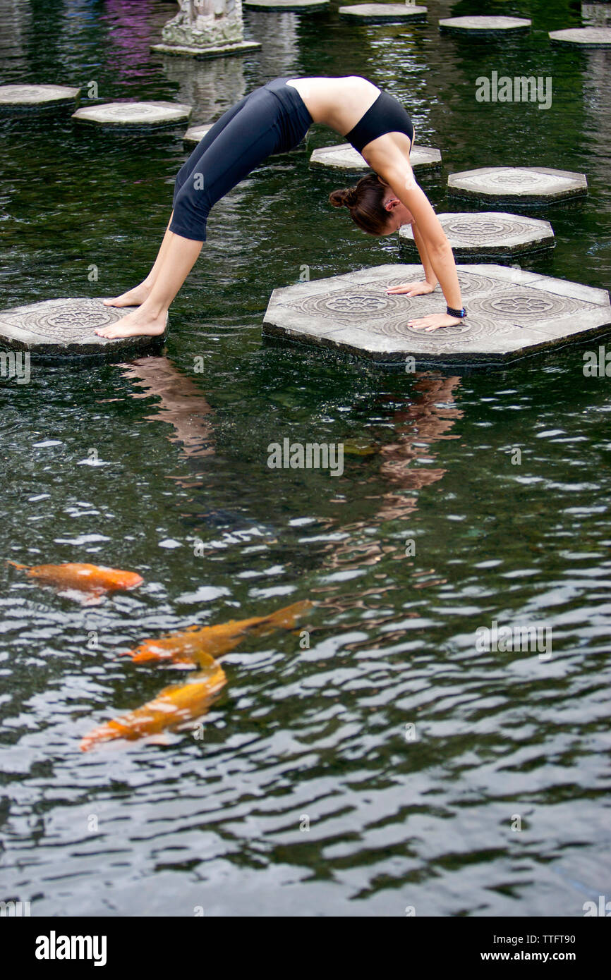 Side view of woman practicing bridge position on platforms amidst pond at park Stock Photo