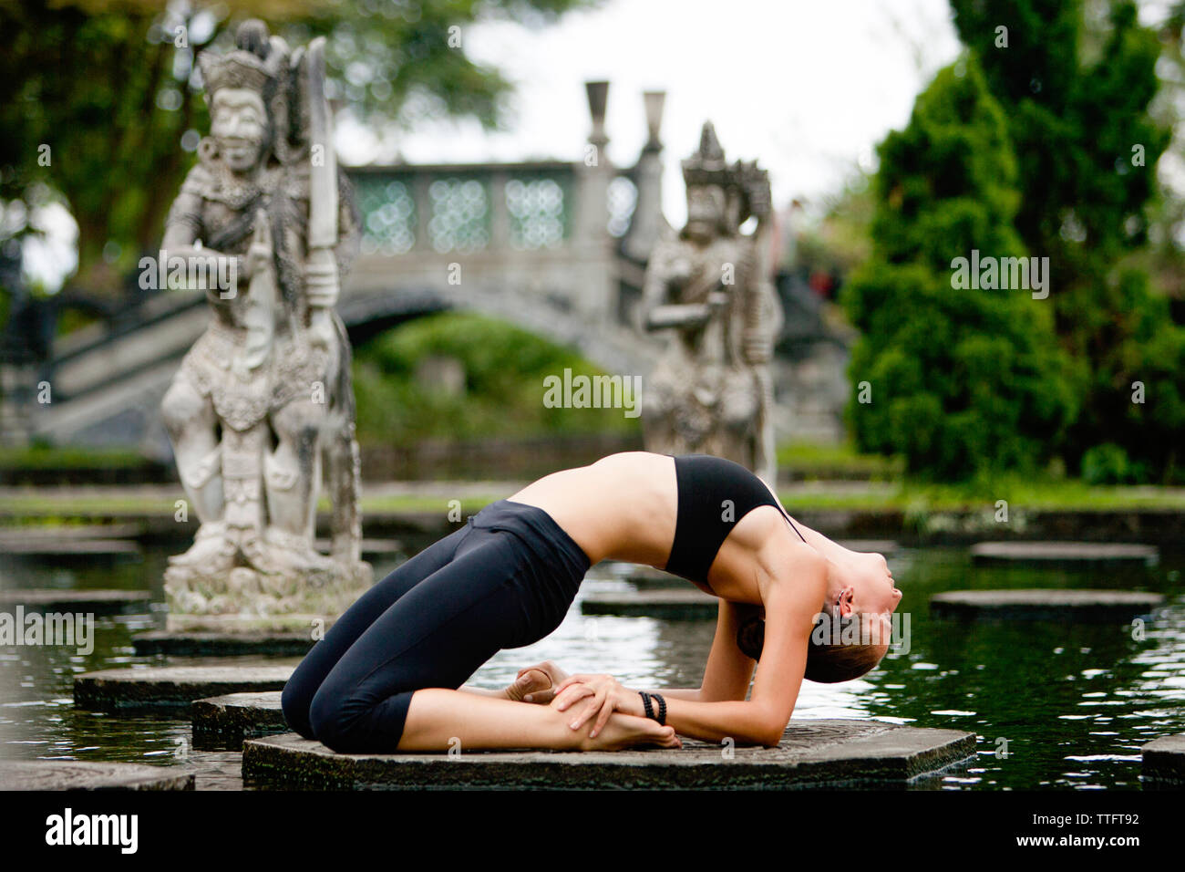 Side view of woman bending over backwards while practicing yoga on platform amidst pond at park Stock Photo