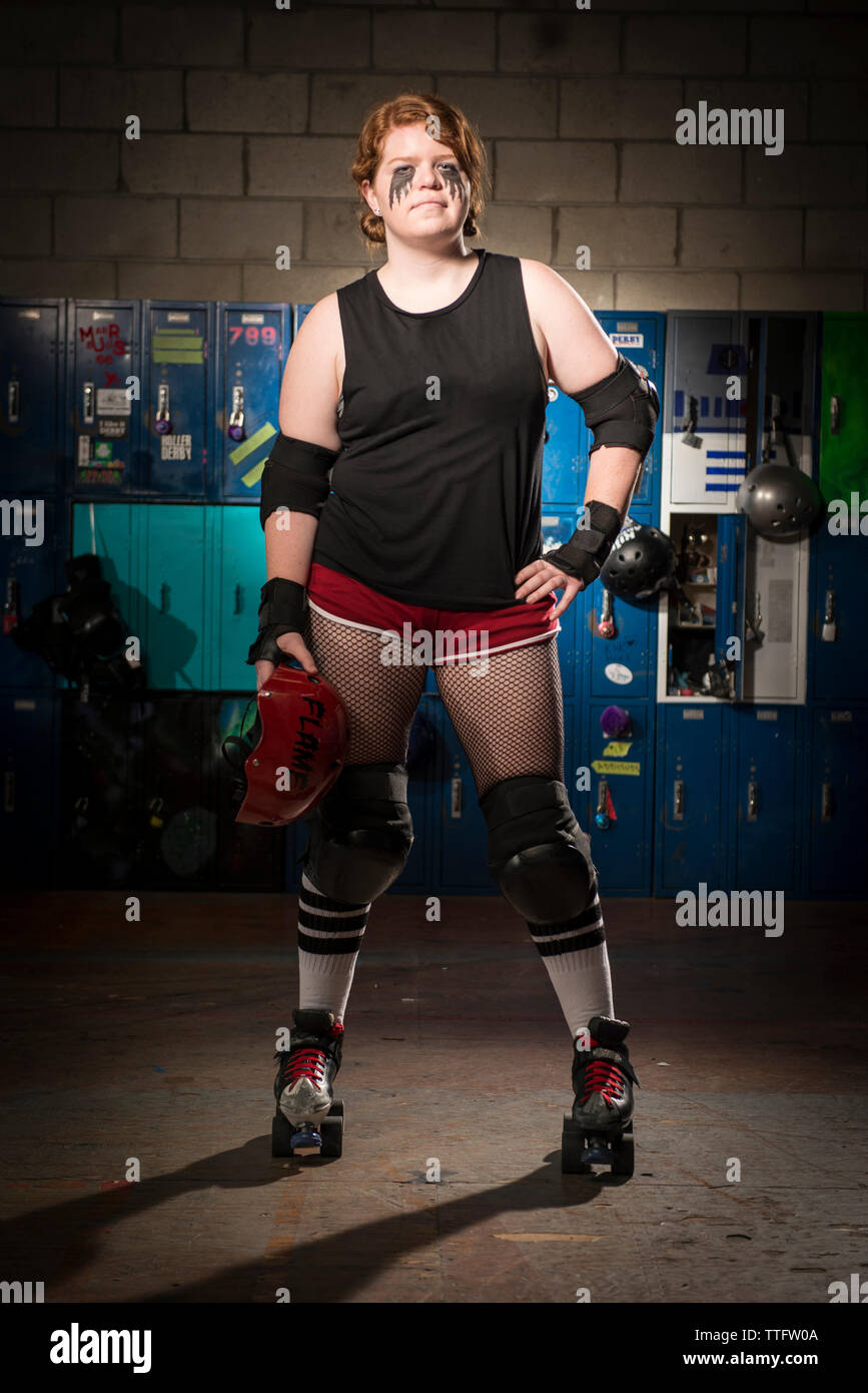 Portrait of confident sportswoman with hand on hip wearing roller skates while standing against lockers Stock Photo