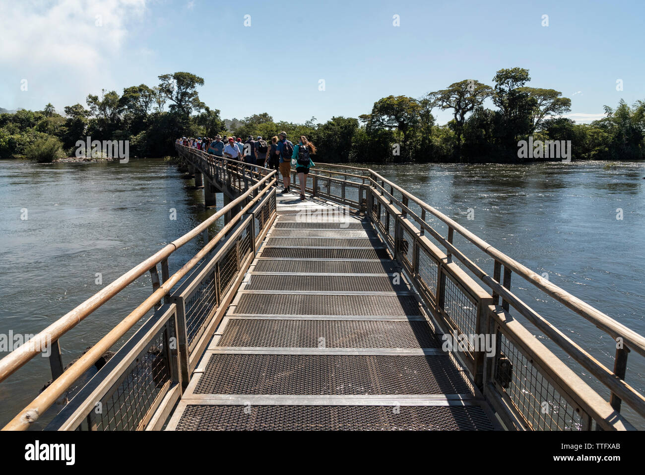 Tourists walking over footbridge on large rainforest river Stock Photo