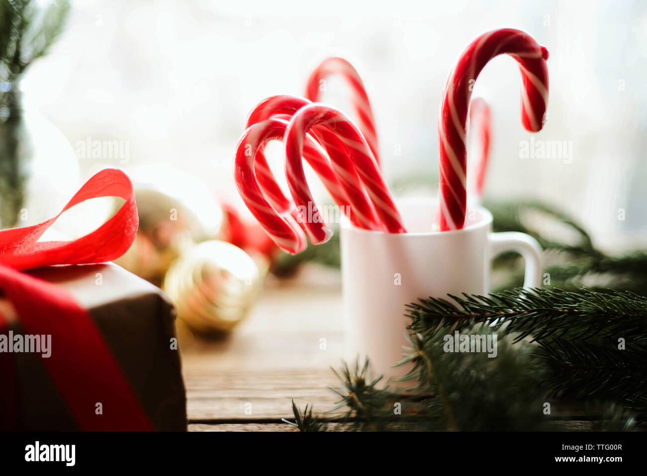 Close-up of candy canes in cup by baubles and twig on wooden table Stock Photo