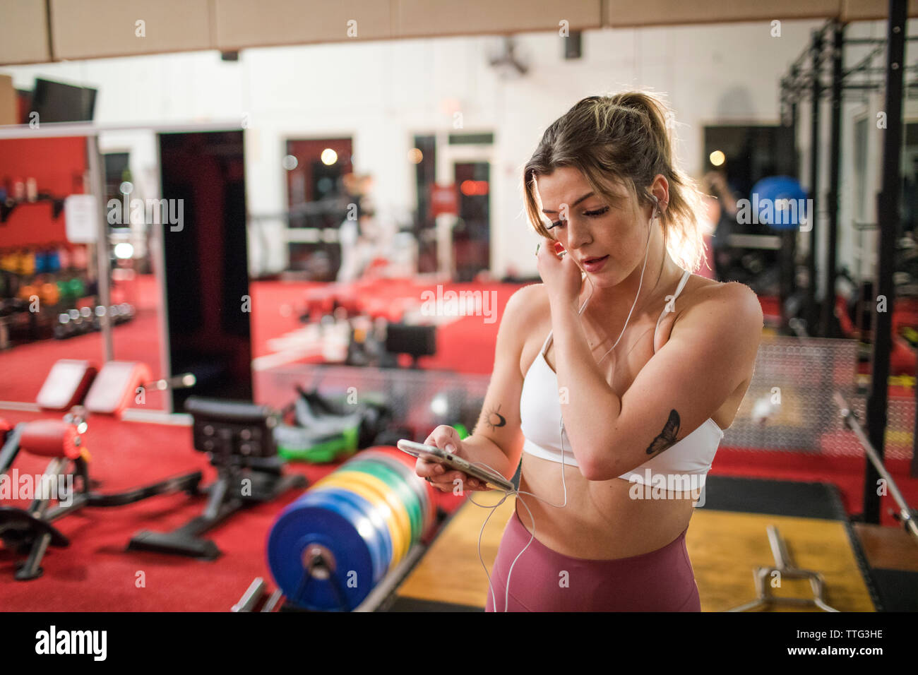 Young woman listening to music with earphones and smartphone at gym Stock Photo