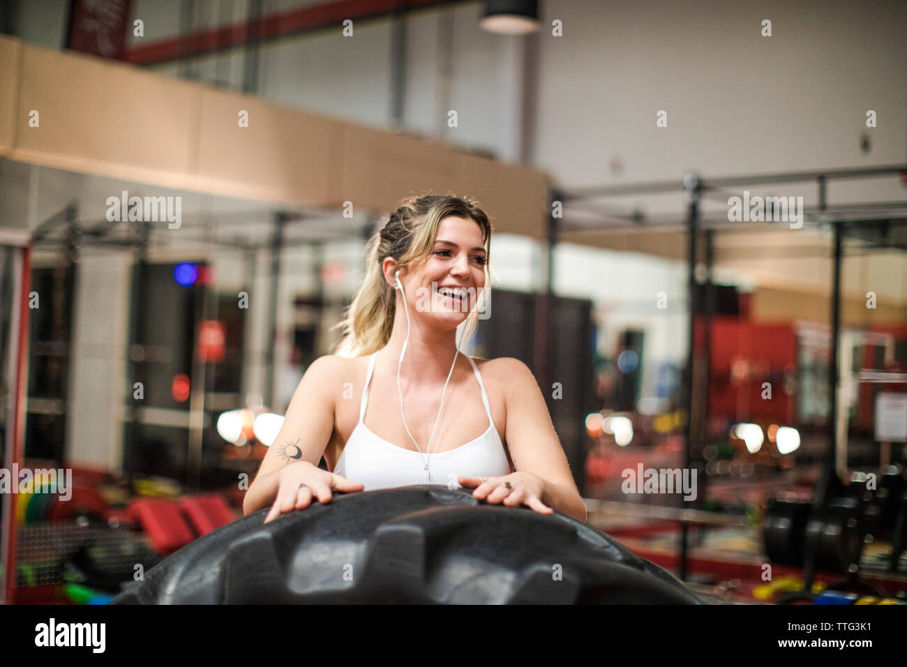 Attractive young woman smiles after lifting heavy tire at the gym. Stock Photo