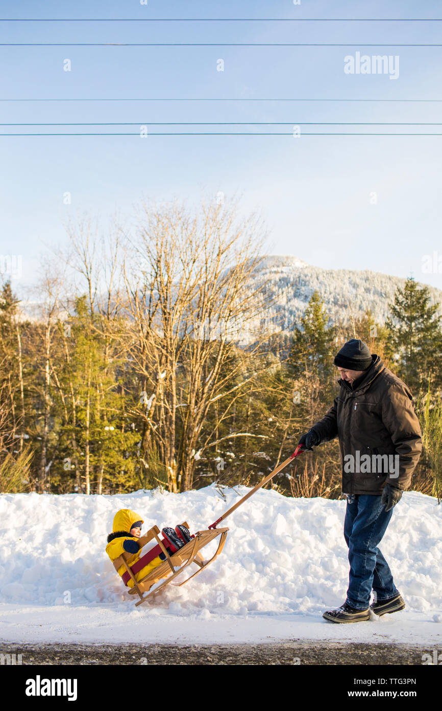 Retired active grandfather pulling his grandson on a wooden sled Stock Photo