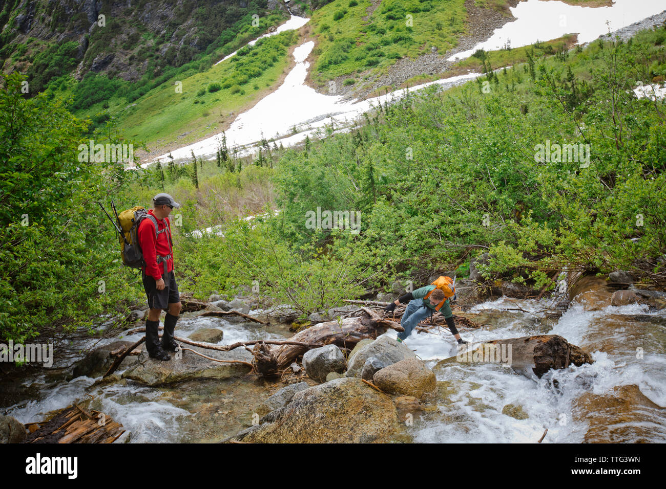 Backpackers carefully crosses a raging river. Stock Photo
