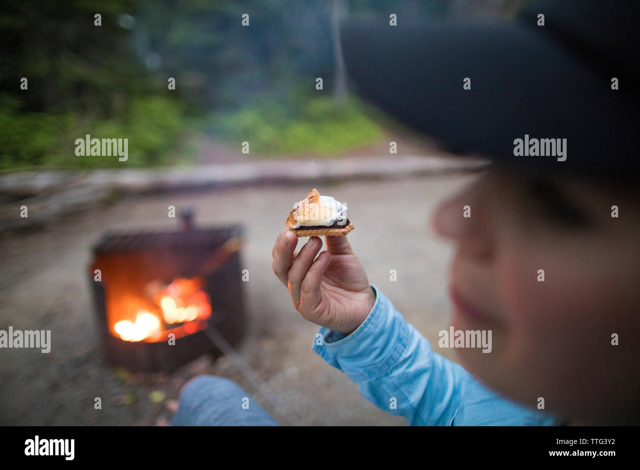 Young woman eating s'mores next to a campfire. Stock Photo