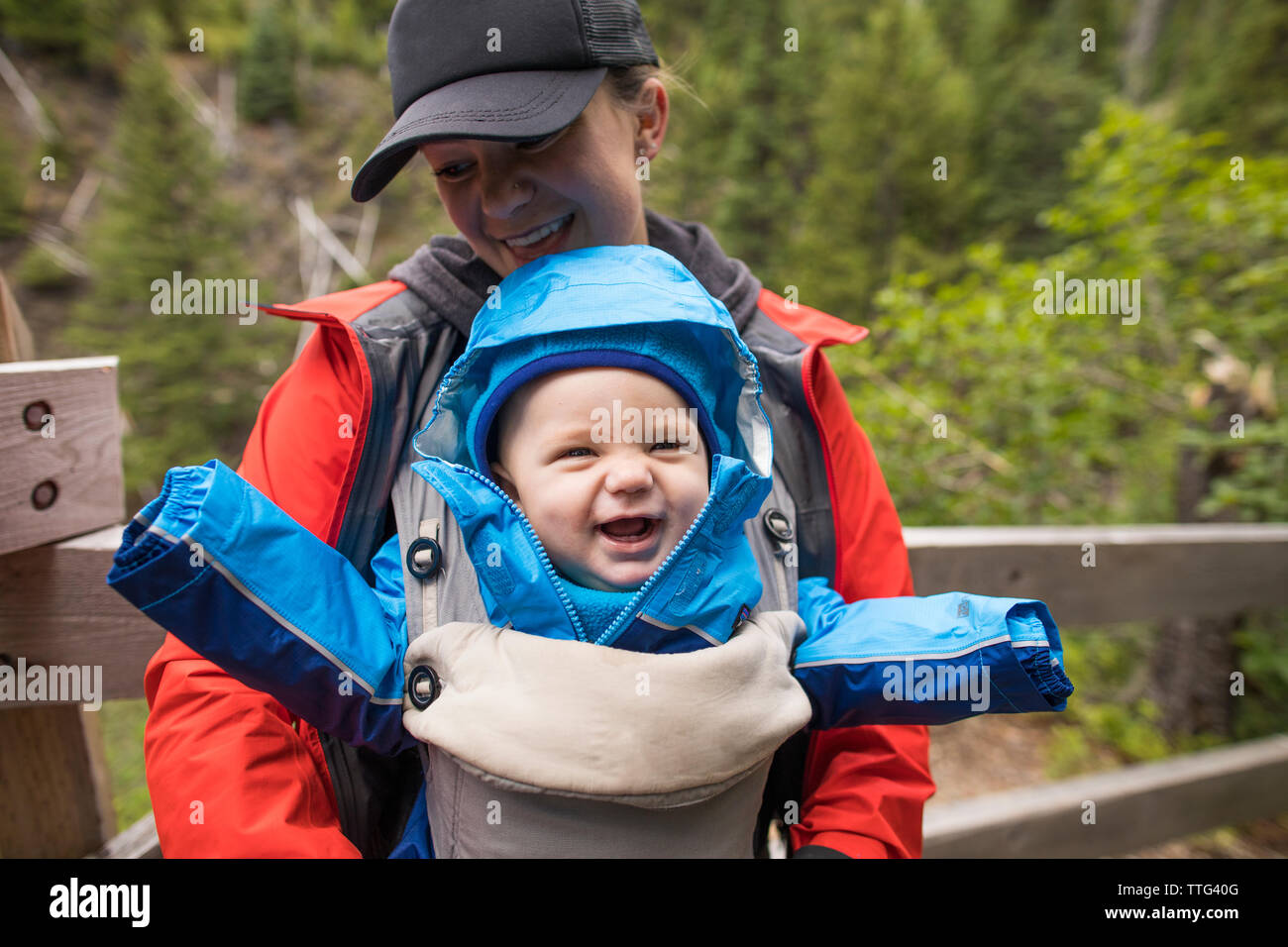 Mother carrying her happy daughter in baby carrier while hiking. Stock Photo