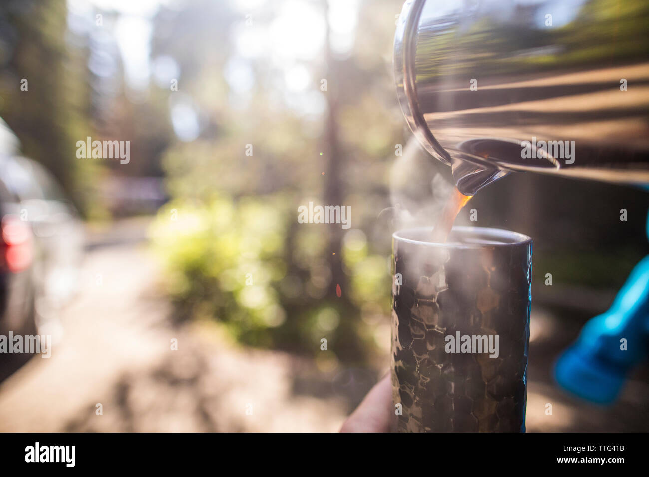 Pouring fresh coffee into a travel mug outdoors. Stock Photo