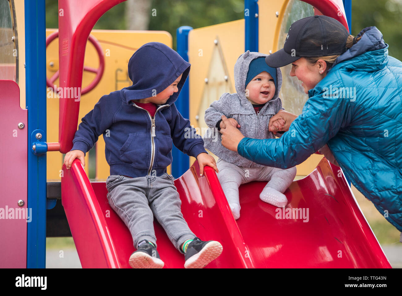 Mother and daughter on playground slide with older brother Stock Photo