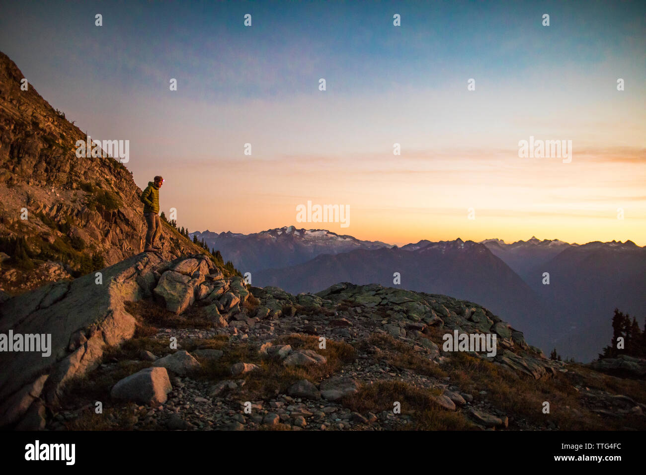 Lone mountaineer standing on rock bluff in mountains at dusk. Stock Photo