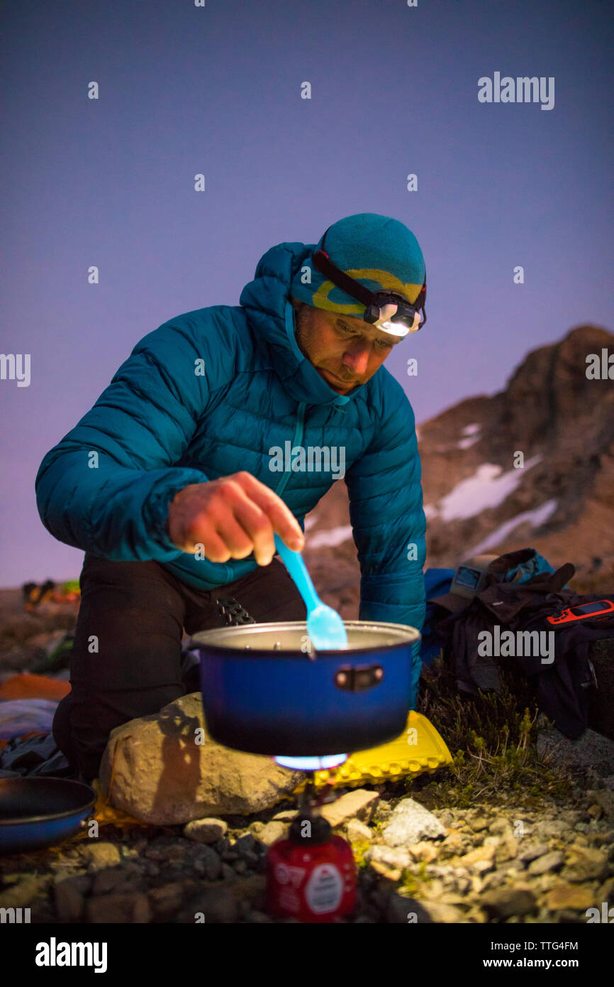 Mountaineer cooking a meal on an ultralight stove in the mountains. Stock Photo