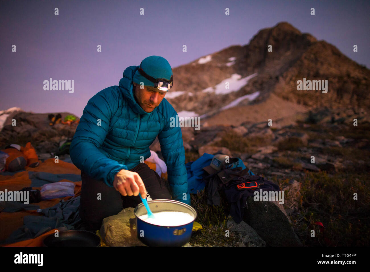 Backpacker cooking on camp stove and using headlamp at sunset Stock Photo