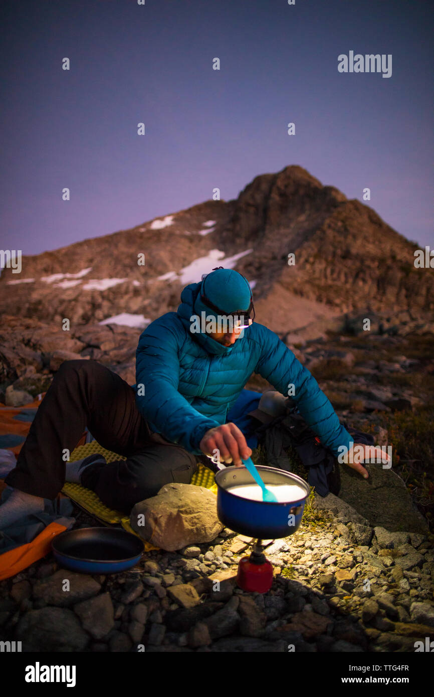 Backpacker cooking on camp stove and using headlamp at sunset Stock Photo