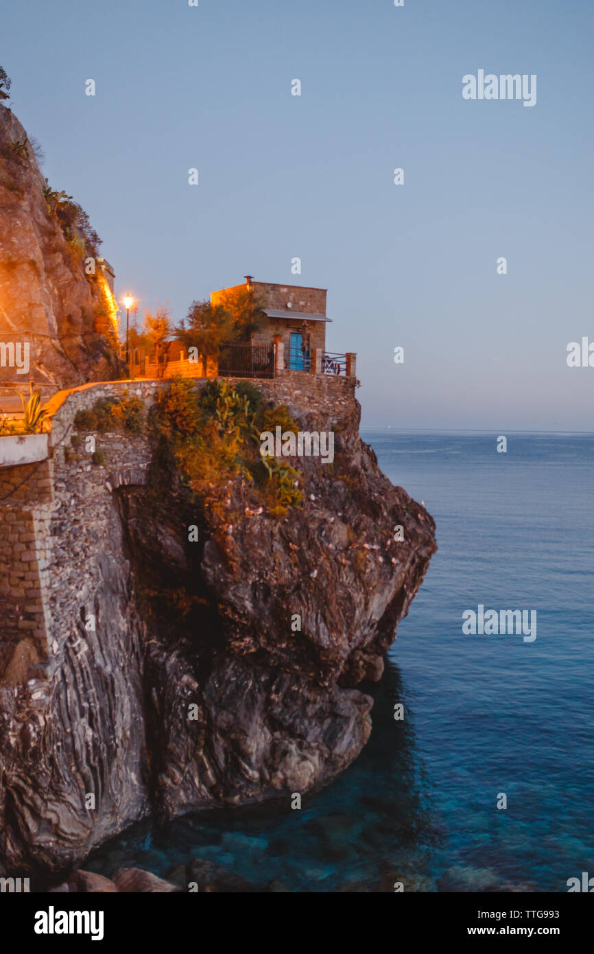 A stone hut atop a rocky ridge overlooking the sea at twilight Stock Photo