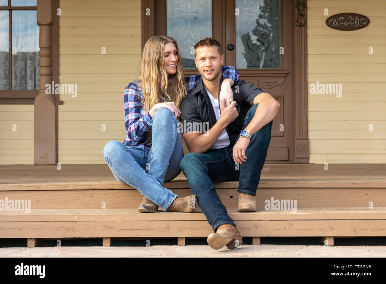 Western wear young couple sitting on front porch of ranch house Stock Photo