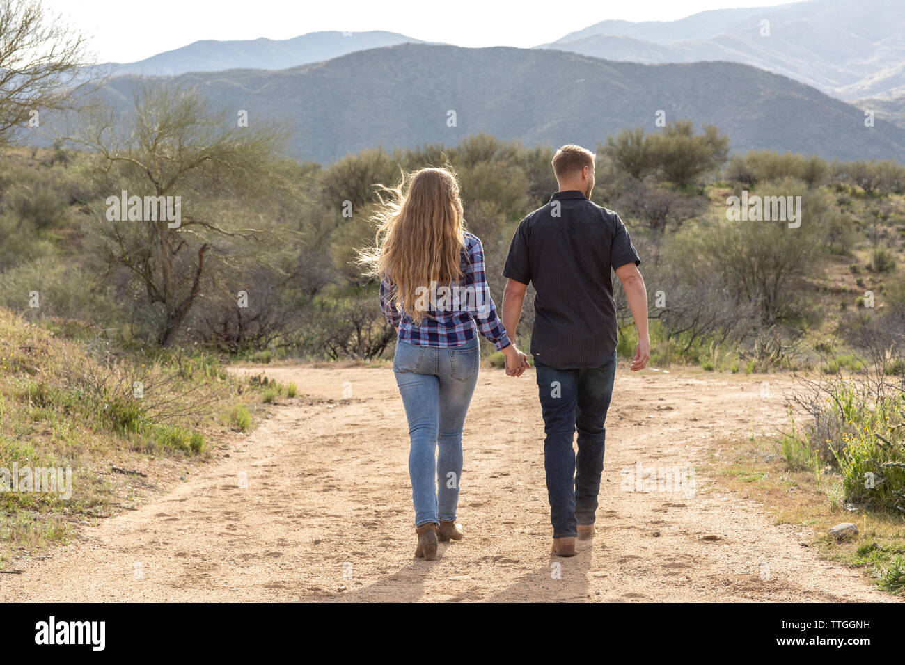 Western wear young couple holding hands and walking in desert Stock Photo