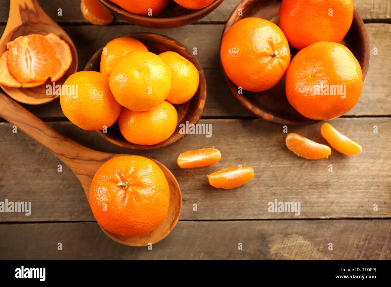 Peeled and unpeeled tangerines in wooden spoons and bowls, top