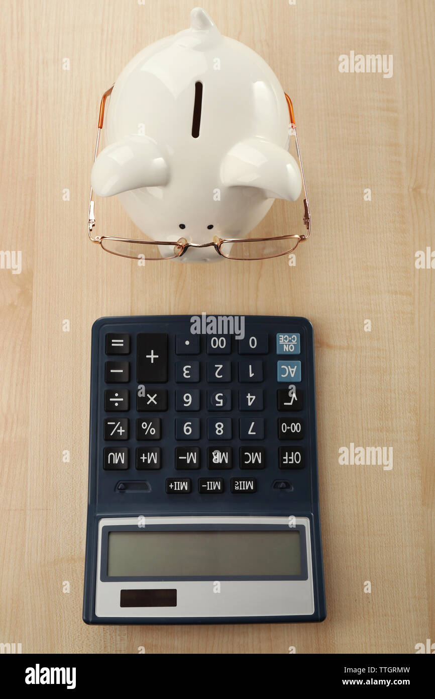 White piggy bank with glasses and calculator on light wooden background ...