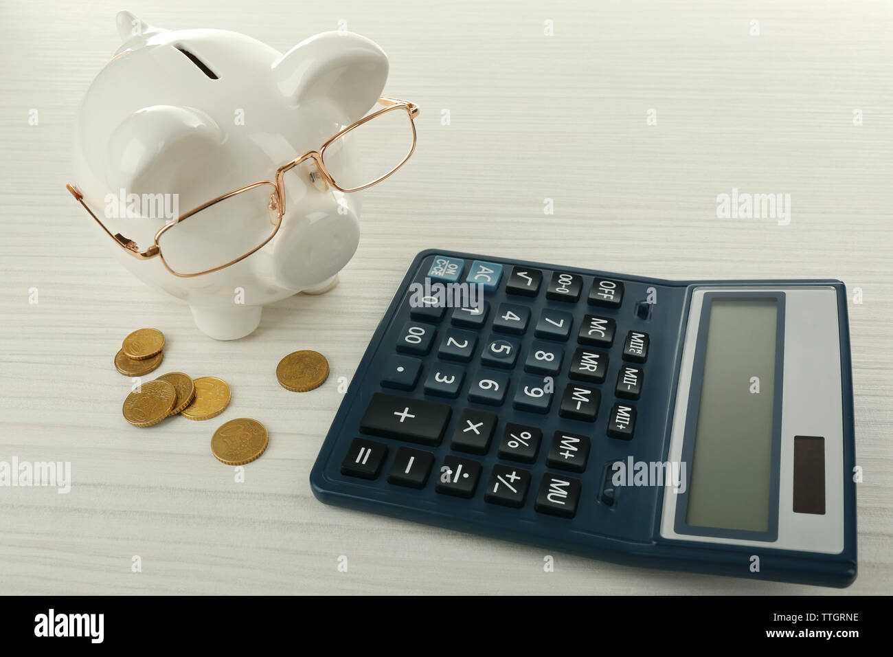 Piggy bank with coins, glasses and calculator on light wooden ...